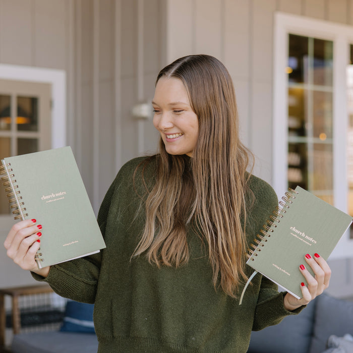 Woman holding two green notebooks with a blurred outdoor patio background