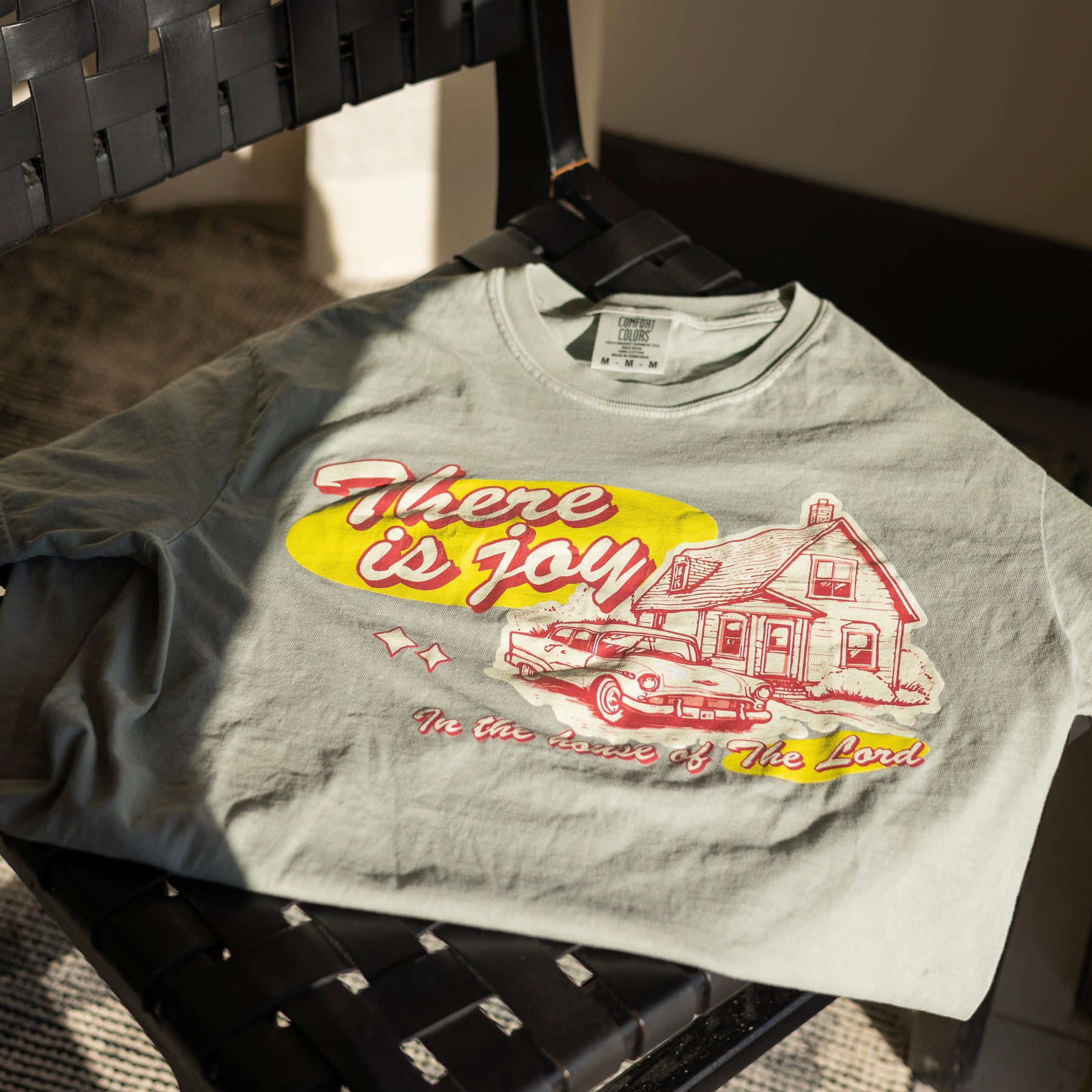 Gray t-shirt with a graphic design featuring a yellow house and text on a chair.