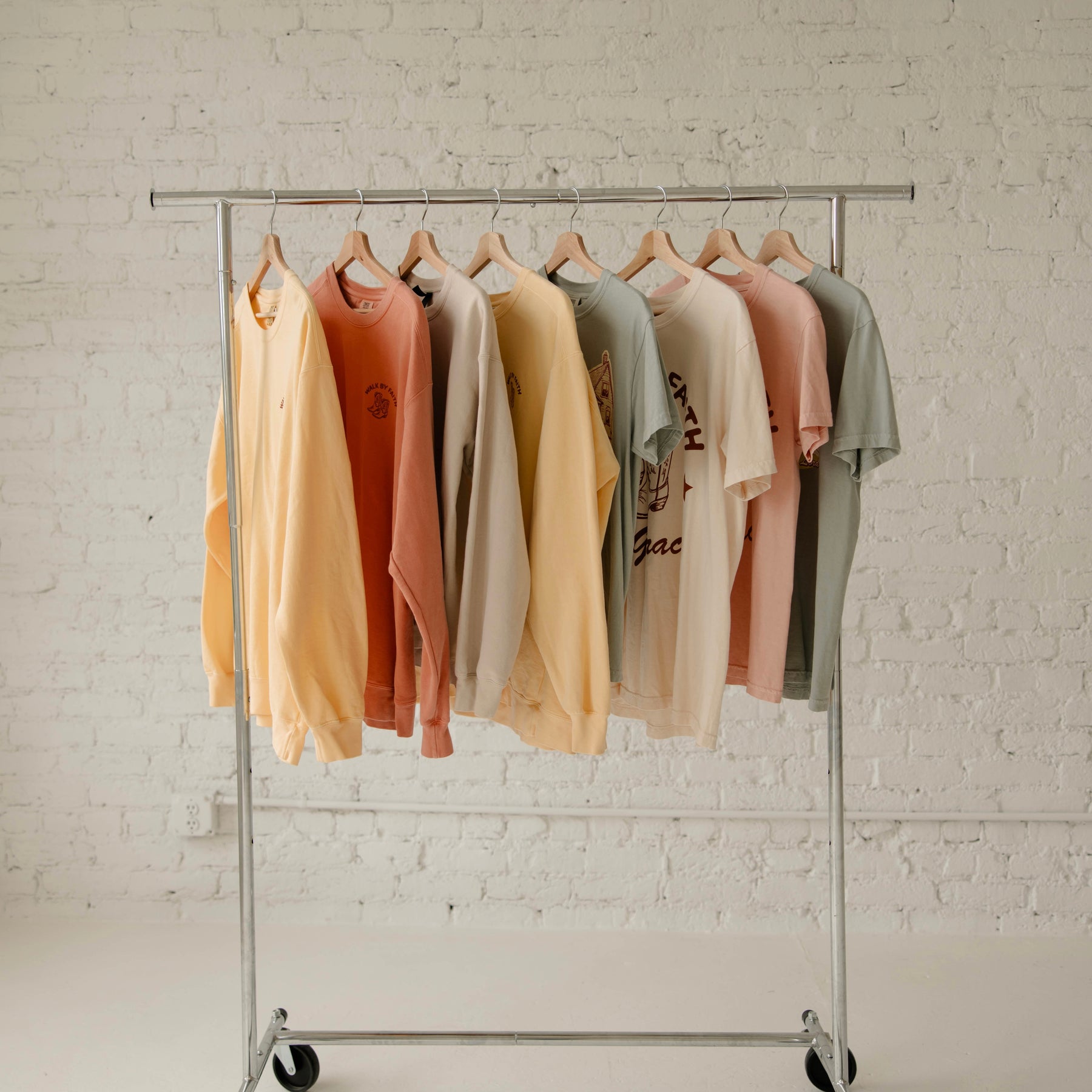 Row of colorful t-shirts on a metal clothing rack against a white brick wall.