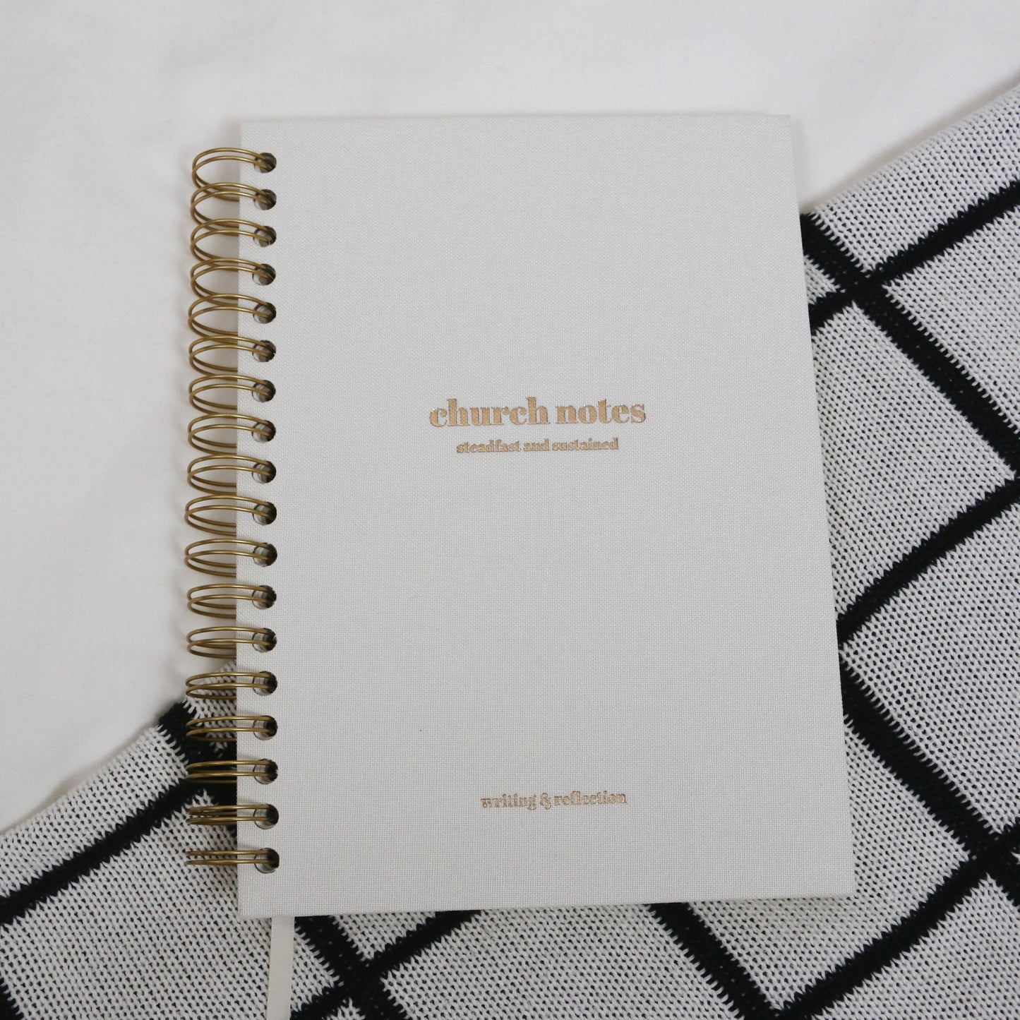 Large 7 x 10" white linen spiral notebook titled 'church notes' 'steadfast and sustained' 'writing & reflection' on a white and black patterned surface