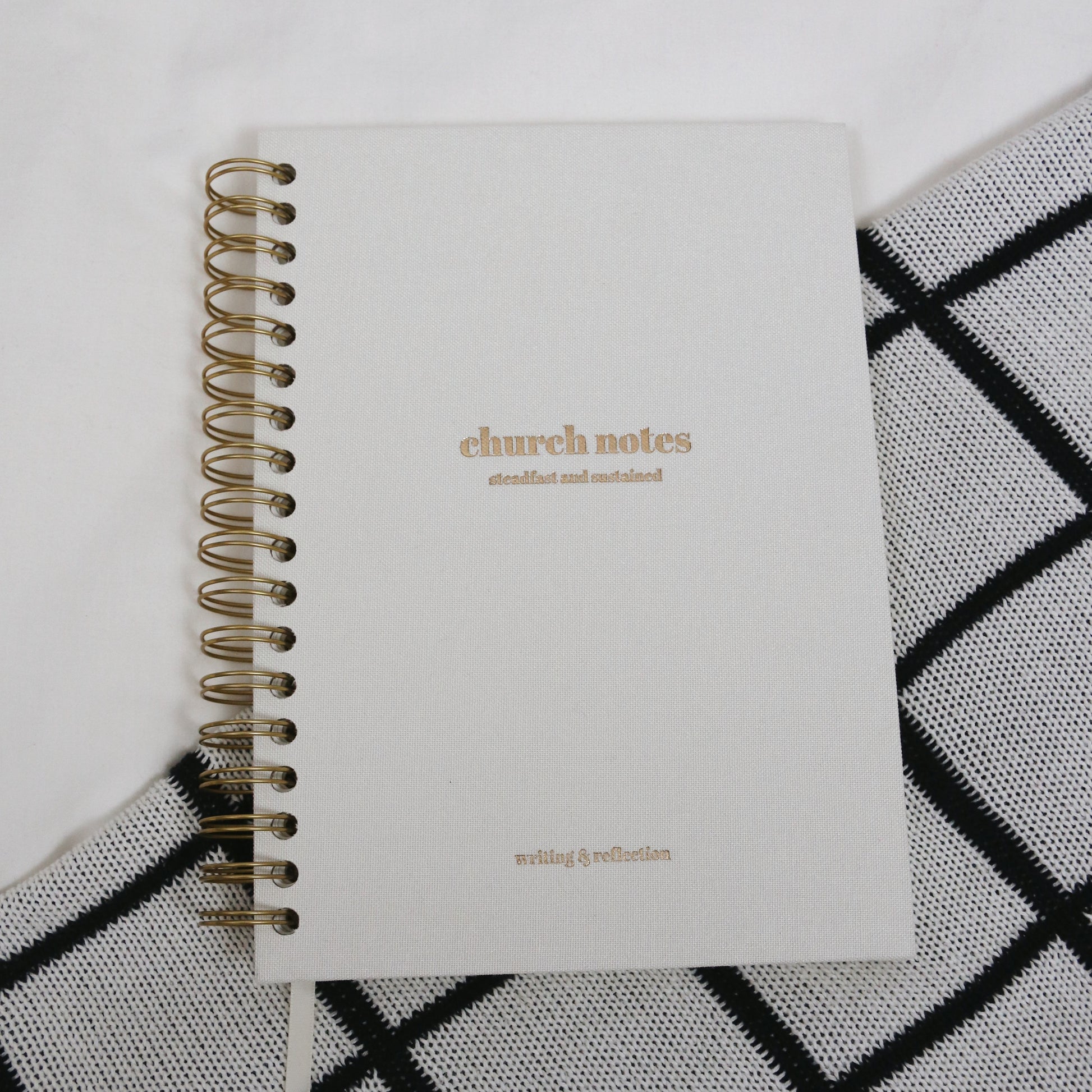Large 7 x 10" white linen spiral notebook titled 'church notes' 'steadfast and sustained' 'writing & reflection' on a white and black patterned surface