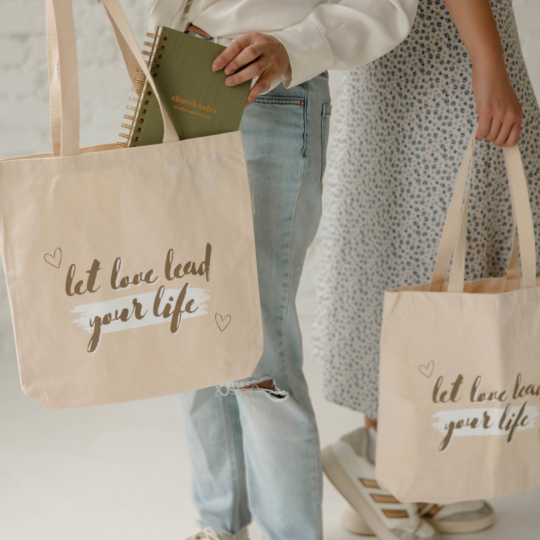 Canvas tote bag with ‘let love lead your life’ text, carrying a green spiral church notes journal, shown in everyday lifestyle setting