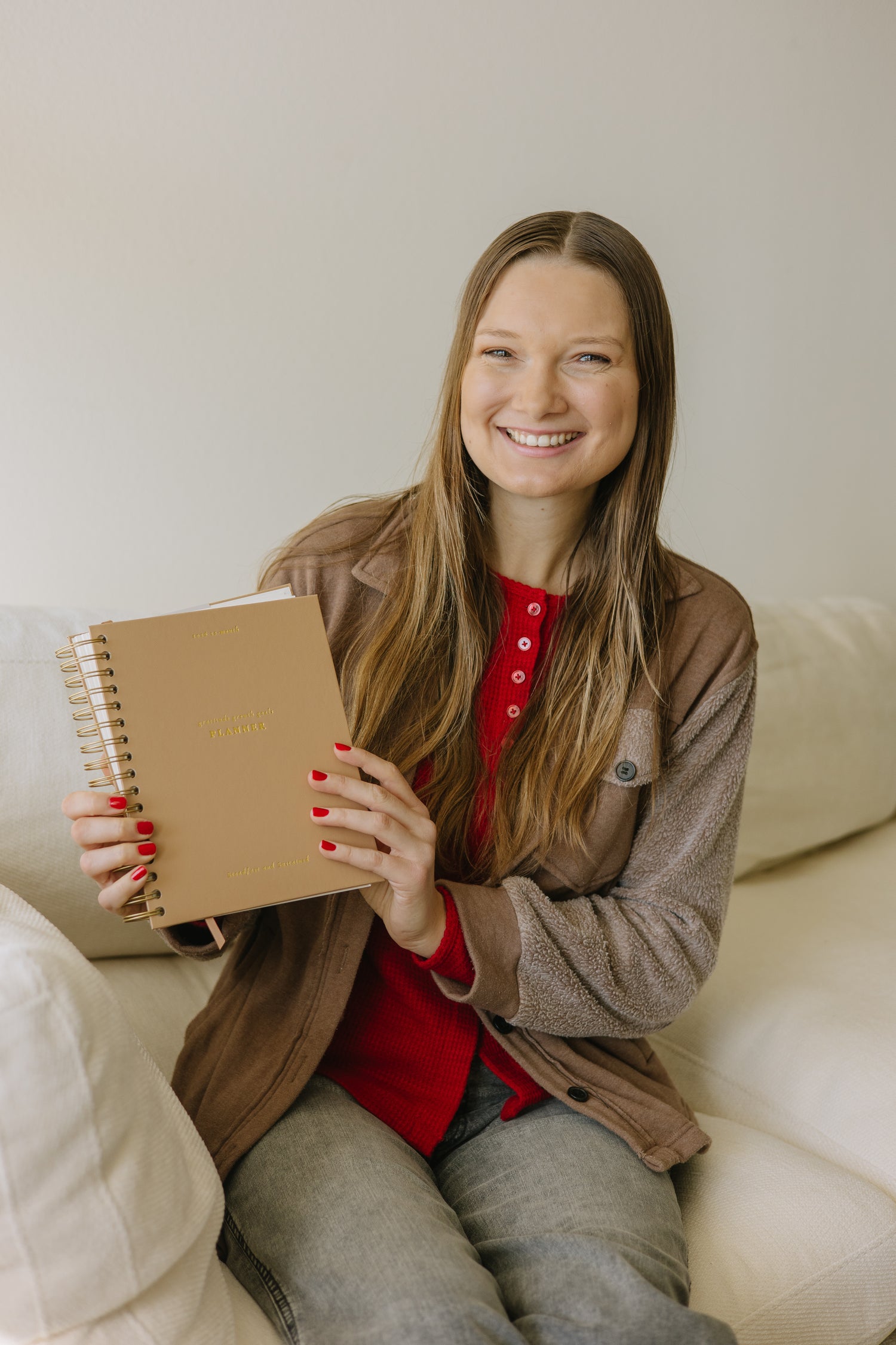 Founder of Steadfast and Sustained holding a faith-based planner journal with spiral binding, sitting on a couch in a cozy home setting
