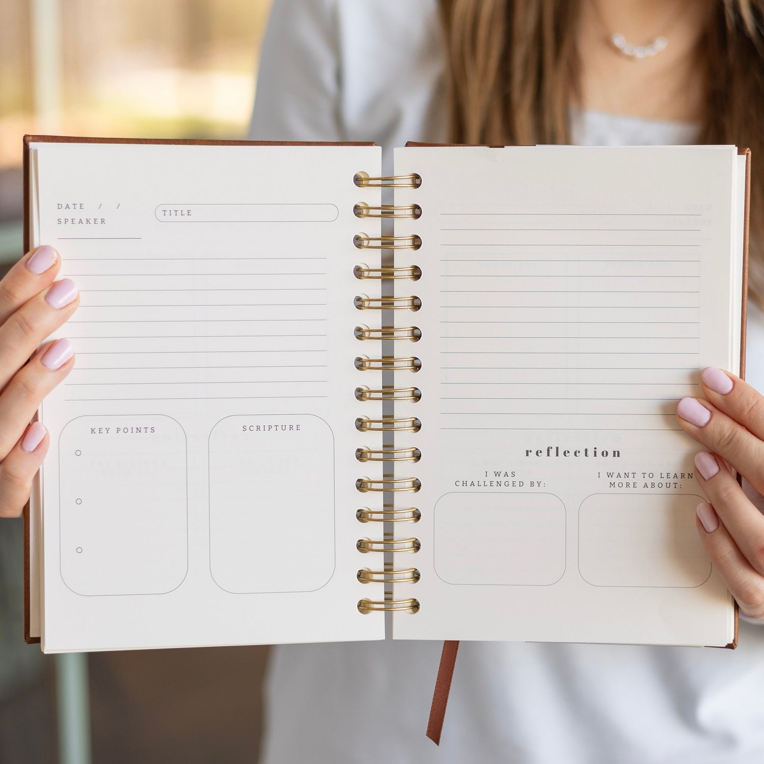 Hands holding open spiral church notes journal showing guided sermon layout with key points, scripture, notes, and reflection sections
